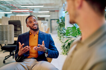 Two businessmen engaged in a project discussion within a modern office, surrounded by vibrant green...