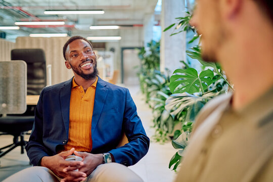 Two businessmen are having a friendly conversation in a bright and modern office space, surrounded by lush green plants