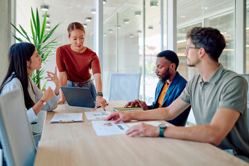 Diverse colleagues analyzing financial charts and reports using laptop, collaborating on project development in workplace
