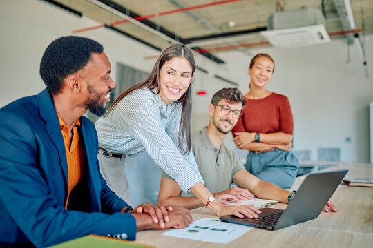 Four businesspeople working together in a modern office, using laptop and documents, collaborating on a project