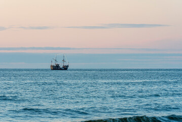 A tourist ship styled like an old galleon sails through the calm waters of the Baltic Sea along the Polish coast, carrying passengers enjoying a scenic maritime journey.