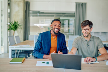 Two smiling business partners collaborating on strategy while discussing ideas and analyzing data using a laptop in a modern office setting