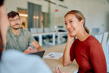 Asian businesswoman smiling and listening to colleagues during a business meeting in a modern office