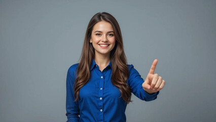 A smiling woman in a blue shirt pointing her finger against a gray colored plain background