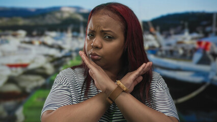 Woman crosses arms in front of docked boats at a bustling port by the seaside under pale morning...