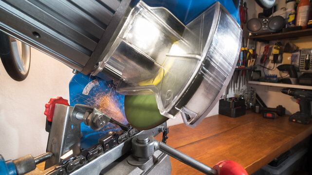 Electric saw chain grinder at sharpening cutting edge of steel tooth on workbench in workroom. Closeup of rotating disc sharp blade with transparent protective cover at grinding by chainsaw sharpener.