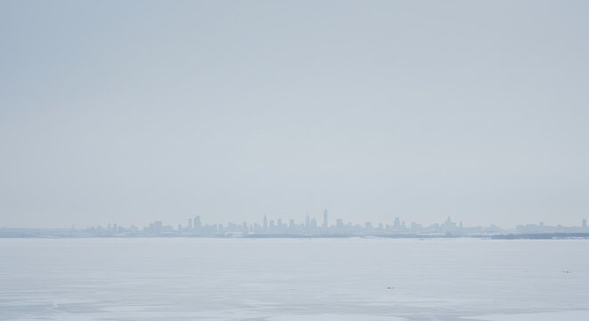 Silhouetted City Skyline Across Icy Water Under Cloudy Sky.