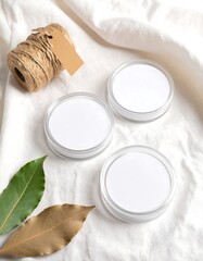 Three Blank Round Containers On White Fabric With Twine And Leaves