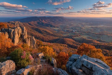 Fototapeta premium Panoramic autumn vista from a mountain peak, with colorful forests and distant hills, a serene valley stretches out towards the horizon under a partly cloudy sky.
