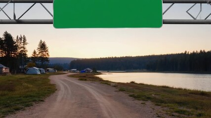 Serene lakeside road leading to a campsite at sunset with tents and trees in the background