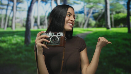 Woman smiling with vintage camera in park under sunlit trees showcasing blissful outdoor photography moment.