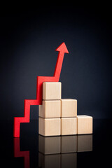 A red upward zigzag arrow next to stacked wooden cubes on a dark background with reflection. . High quality photo