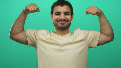 Fototapeta premium Young hispanic man flexing bare forearms and clenched fists in a bright green studio space; confidence motivation empowerment resilience.