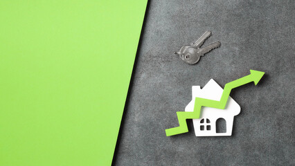 A white house model with a green upward arrow, symbolizing rising property value, next to keys on a...