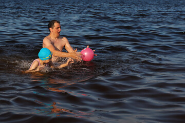 Dad and daughter are happily playing ball in water and swimming