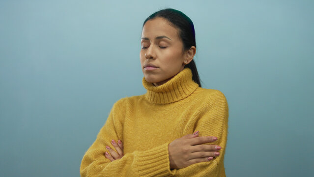 Woman wearing yellow sweater stands isolated against a solid blue background with a thoughtful expression, suggesting introspection or contemplation in a studio setting. - Powered by Adobe