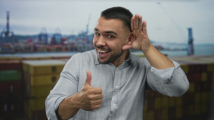 Man cups ear with hand by his head at a building overlooking a busy port area while smiling...