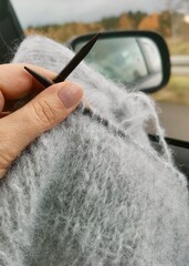 Cozy travel moment: woman knitting in the car with scenic countryside outside the window. A peaceful blend of creativity, road trip, and relaxation.
