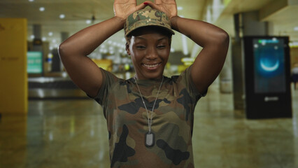 Woman in camouflage uniform raises arms showing dogtag while standing in busy airport; pride duty...