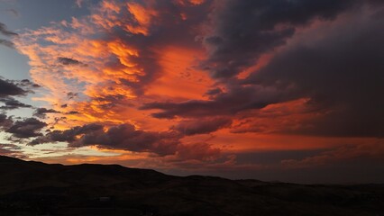 Aerial view of a dramatic sunset sky ablaze with fiery orange hues contrasting against the dark, rolling hills below, Reno, Nevada, United States.