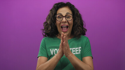 Woman volunteer in green uniform happily clapping with a joyful expression against an isolated pink background