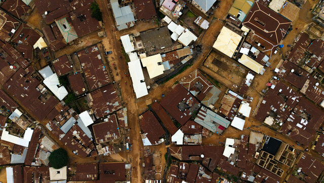Aerial view of a dense urban landscape showcases rusty corrugated rooftops interspersed with brighter structures, creating a textured tapestry of urban life, Jos, Plateau, Nigeria.