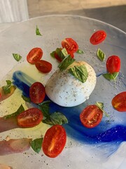 Closeup image of a caprese salad on a glass plate being held by a woman’s hand