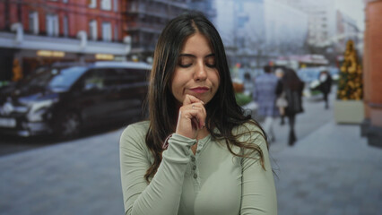 Fototapeta premium Woman contemplating while standing on a busy city street surrounded by buildings and vehicles, indicating an outdoor urban setting filled with pedestrians.