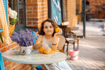 Cute child girl sits in outdoor cafe with oranges fruits. Provence.