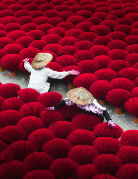 Aerial view of artisans amidst a sea of vibrant red incense sticks drying under the sun, creating a striking visual tapestry, Quang Phu Cau, Hanoi, Vietnam.