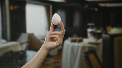 Male hand holding a beauty blender in a dimly lit upscale restaurant with blurred white table...