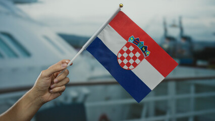 Hand holding croatian flag on a boat during a seaside cruise, symbolizing national pride in an...