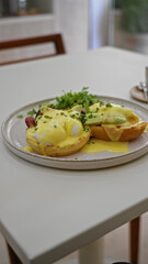 Person enjoying delicious eggs benedict with avocado indoors at a cozy restaurant with a fork and knife on a white table featuring fresh ingredients and bright daylight.
