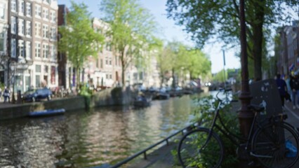 Fototapeta premium Blurred canals of amsterdam with defocused bicycles and lush greenery lining the waterways on a sunny day, capturing the essence of the netherlands' charming capital.