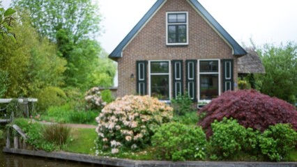 Front view of charming house with blurred greenery and flowers creating a serene, scenic atmosphere with focus on architectural detail and landscaped garden.
