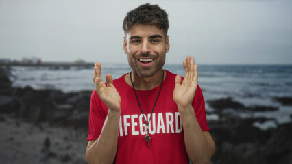Smiling bearded hispanic young lifeguard man claps hands on beach under blue sky; happiness pride duty.