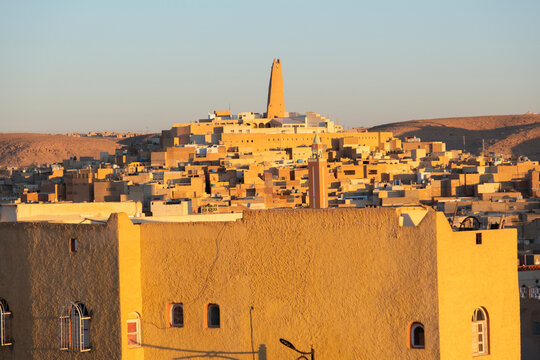 View of city with mud-brick dwelling and tall minaret against clear sky, Algeria, Ghardaia