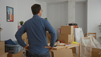 Mature man in new home surrounded by moving boxes as he surveys his living room while decorating his apartment and planning furniture layout during a moving day.