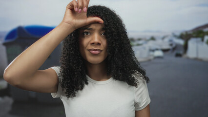 Woman makes l sign with hand on forehead while standing in front of a recycling container on street...