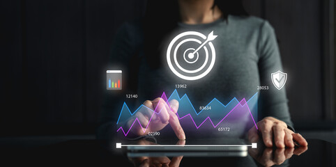 A woman interacts with a digital tablet displaying graphs and targets, representing data analysis and strategic planning.