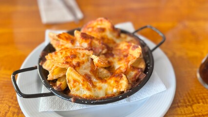 Fototapeta premium Hot Cheesy Potato Wedges Fresh from the Oven Served in a Rustic Pan on Wooden Table
