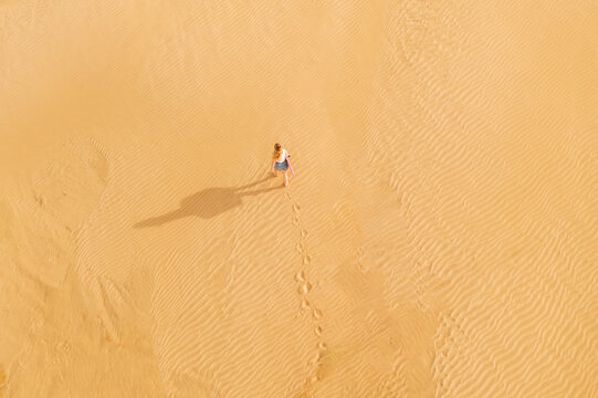 Aerial view of a lone figure casting a long shadow as they traverse the undulating dunes, footprints trailing behind them, Whangarei, Northland Region, New Zealand.