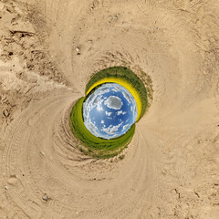 creative tiny planet photo of a rural landscape with dirt road, green fields, and cloudy sky forming a circular world.
