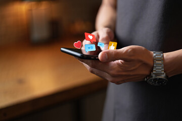 Close up of a man's hands using a smartphone for social media engagement with floating icons