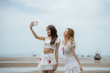 Two women are standing on a beach, one of them taking a picture of the other with a cell phone