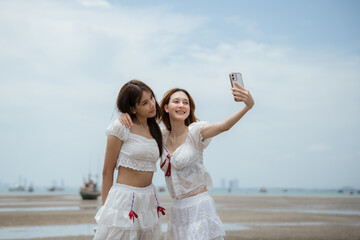Two women are standing on a beach, one of them taking a picture of the other with a cell phone