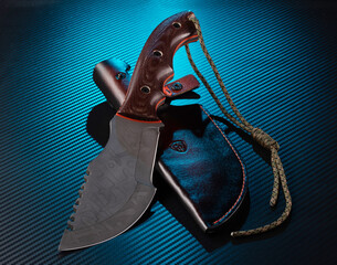 Large hunting knife with saw blade and leather sheath on blue background.