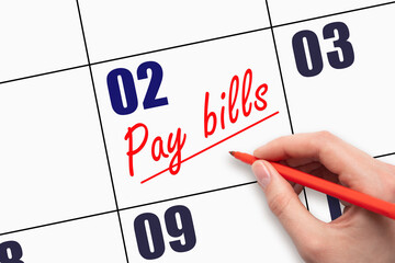 2nd day of the month.  Hand writing Pay bills reminder and drawing a line on calendar with red pen...