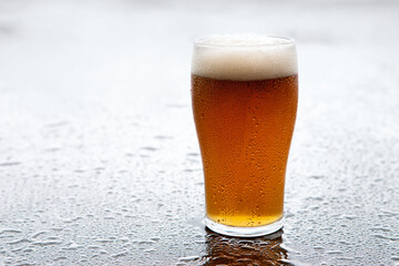 a glass of beer sitting on a wet surface