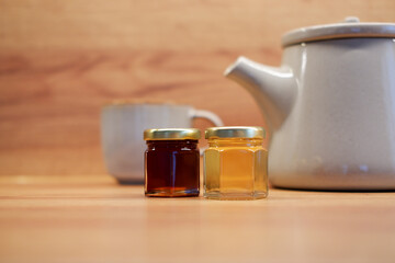 Small glass jars of honey next to ceramic teapot. Warm natural light and cozy food concept.